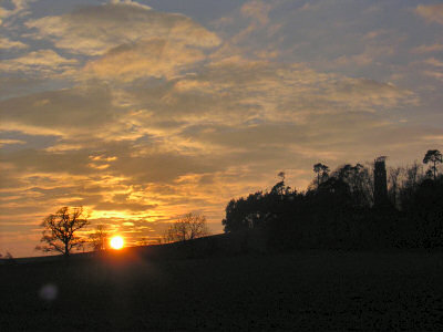 Picture of a sunset behind a hill with a tower