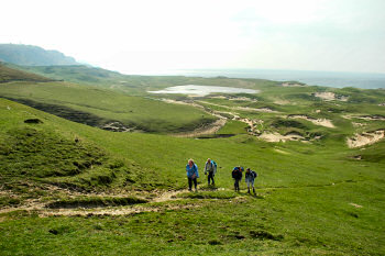 Picture of walkers walking up some dunes, sea in the background