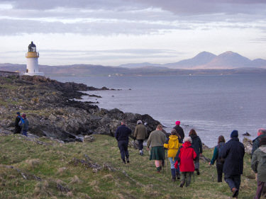 Picture of walkers on a shore approaching a lighthouse