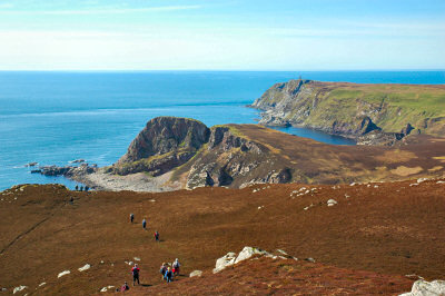 Picture of walkers on cliffs high above the sea, a monument visible in the distance