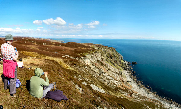 Picture of a panoramic view of walkers sitting on a cliff overlooking the sea