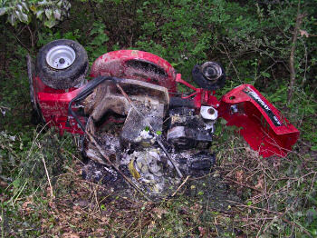 Picture of a partly burned lawnmower lying on the side in a ditch
