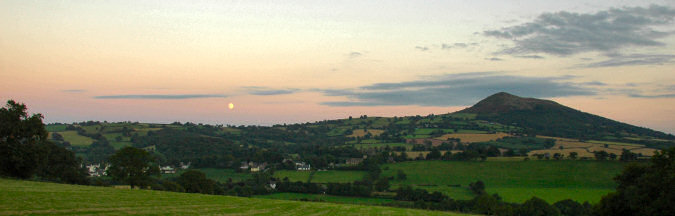 Picture of the moon rising over a village and a hill