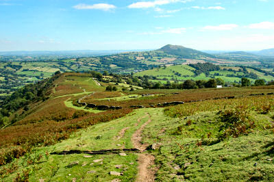 Picture of a view down a hill over a wide landscape with another hill in the distance (Ysgyryd Fawr / Skirrid from Hatterrall Hill)