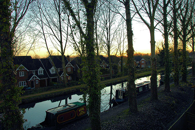 Picture of a sunset over a canal lined with trees, the sun has just disappeared