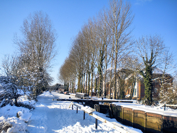 Picture of a canal lock and tree lined canal path after heavy snowfall
