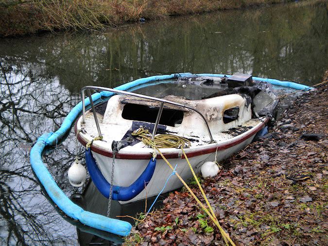 Picture of a burned out small sports boat surrounded by a swimming barrier
